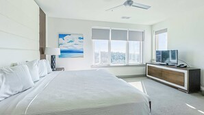 A modern hotel room with a large bed, a TV on a wooden cabinet, and a ceiling fan. - Pool-view condo with on-site pool, hot tub, roof deck, gym, & balcony (Inlet Beach)