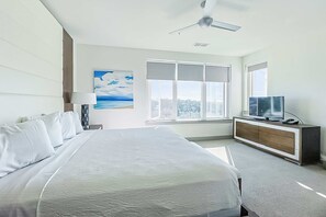A modern hotel room with a large bed, a TV on a wooden cabinet, and a ceiling fan. - Pool-view condo with on-site pool, hot tub, roof deck, gym, & balcony (Inlet Beach)