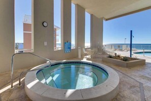 A hot tub with a view of the ocean, surrounded by a pool and lounge chairs. - Beachfront condo with balcony view & pool - snowbird-friendly (Panama City Beach)