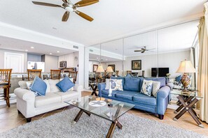 A spacious living room with a sofa, coffee table, and a ceiling fan. - Beachfront condo with balcony view & pool - snowbird-friendly (Panama City Beach)