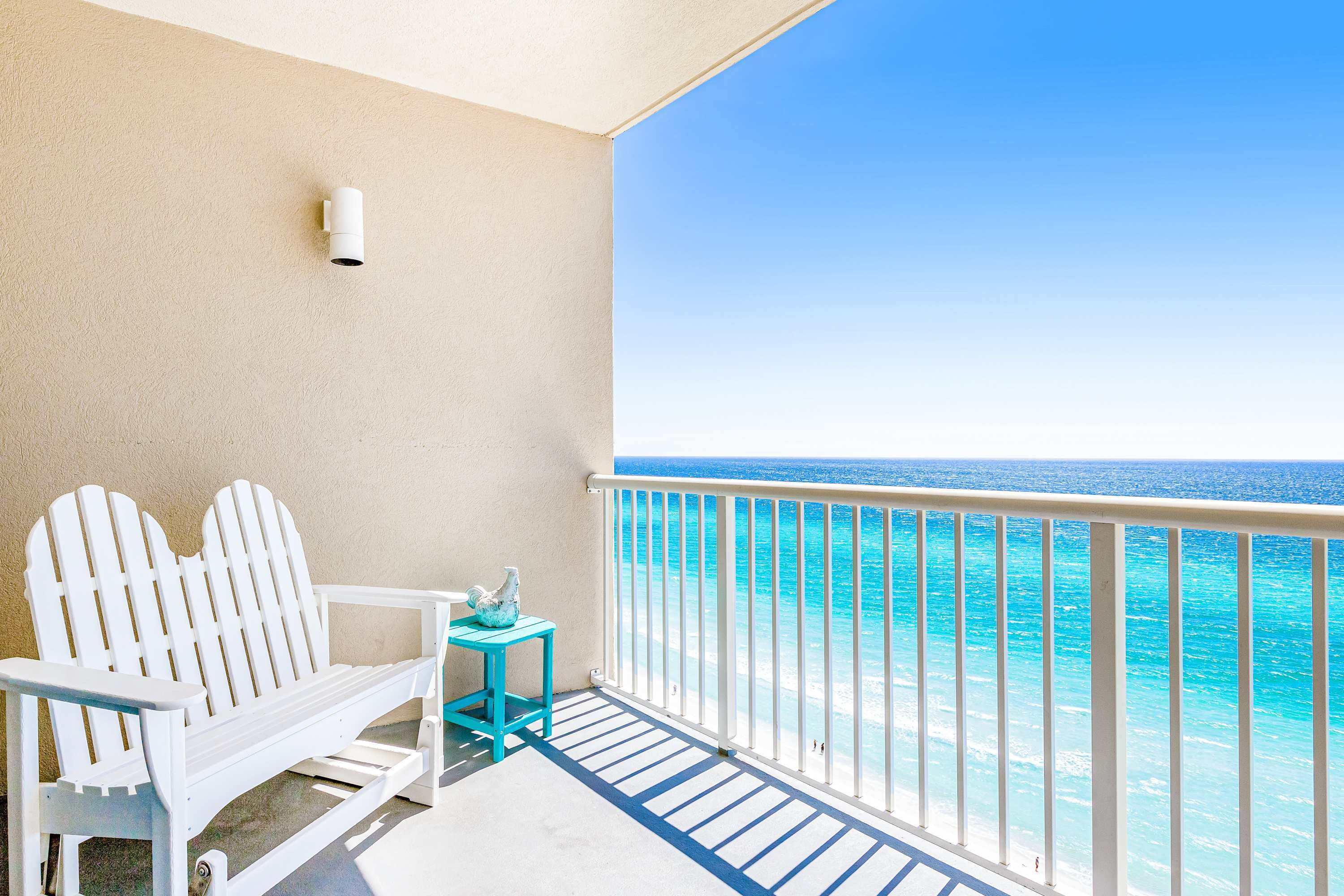 Un balcon avec un fauteuil Adirondack blanc, une petite table turquoise et une vue sur l’océan.