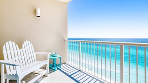 En balkon med en hvid Adirondack-stol, et lille turkis bord og udsigt til havet.