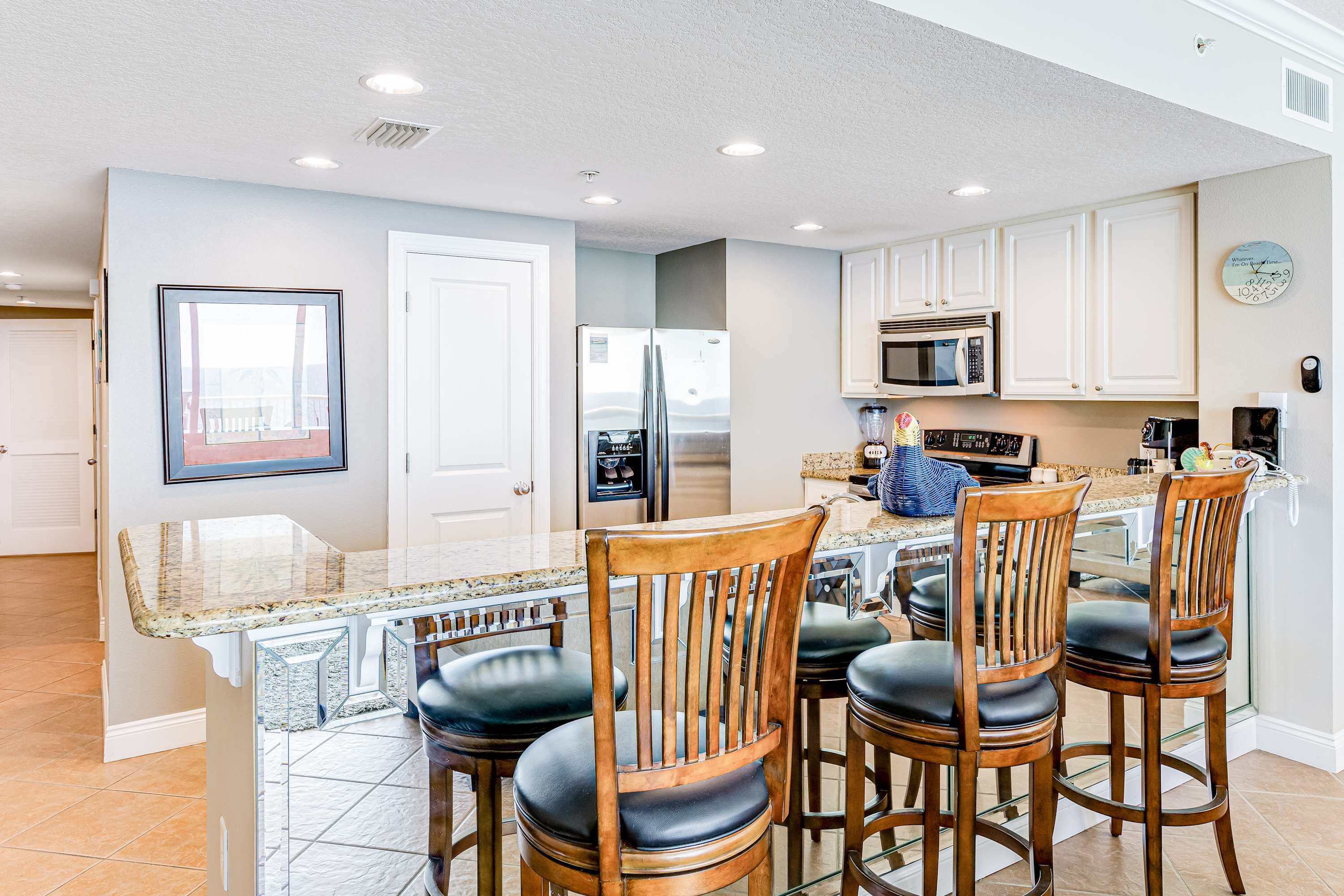 A kitchen with white cabinets, a stainless steel refrigerator, a microwave, and a granite countertop.