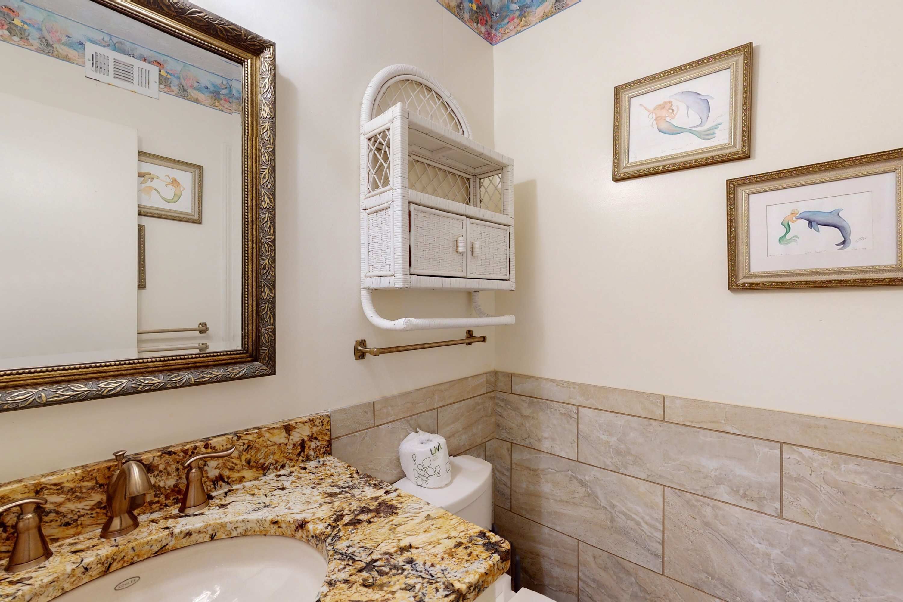 Un bagno con lavabo in marmo, un ampio specchio, uno scaffale in vimini bianco e opere d'arte incorniciate alle pareti.