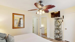 Une chambre à coucher avec un grand lit, un ventilateur de plafond, une télévision et un miroir décoratif.