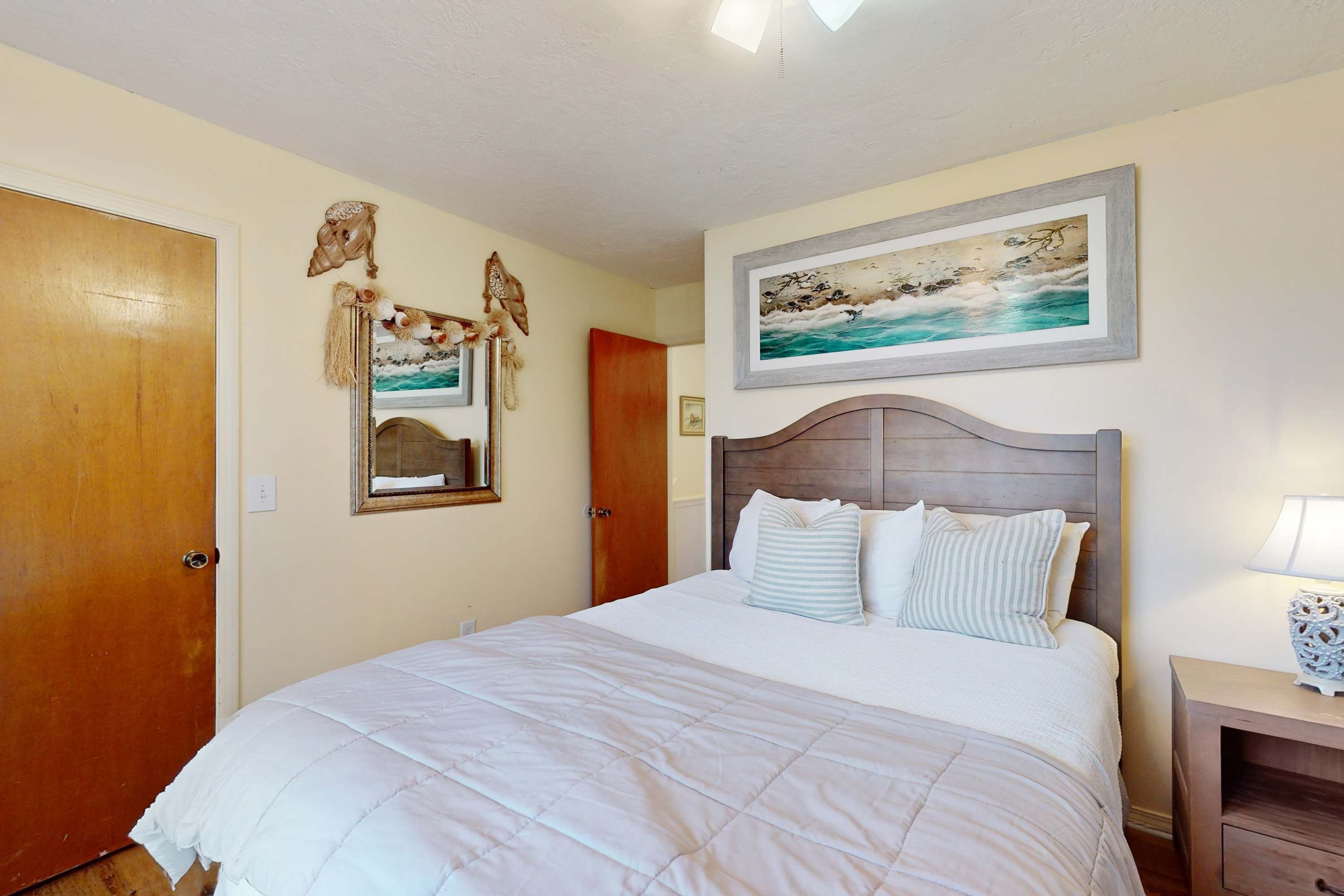 A bedroom with a large bed, wooden headboard, and a painting of a seascape.