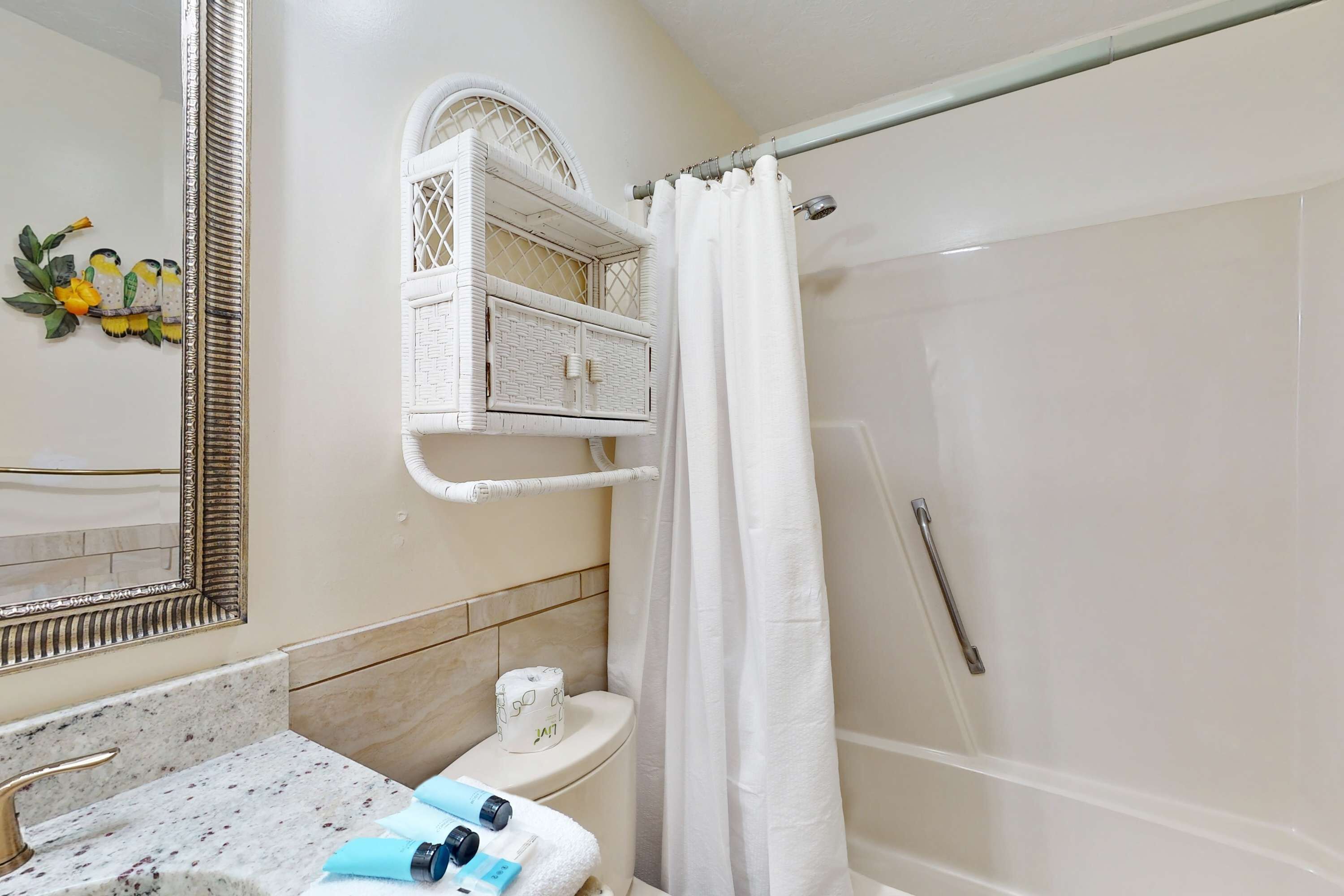 Un baño con lavabo de mármol, inodoro con cesta, cortina de ducha y espejo con marco decorativo.