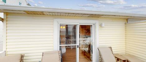 A covered patio with two lounge chairs and a table, a sliding glass door leading to an interior room, and a white exterior wall.