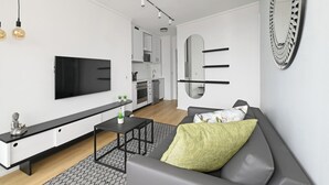 A modern living room with a flat-screen TV, a sofa, a coffee table, and a kitchen in the background. - The Flamingo | Sea Point Prom | One Bed | Balcony (Cape Town)