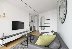 A modern living room with a flat-screen TV, a sofa, a coffee table, and a kitchen in the background. - The Flamingo | Sea Point Prom | One Bed | Balcony (Cape Town)