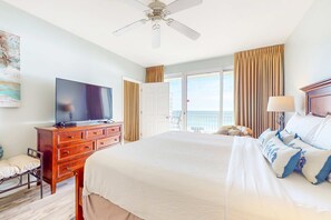 A hotel room with a large bed, a television on a wooden dresser, a balcony with curtains, and a ceiling fan. - Modern condo w shared pool & fitness center - close to the beach (Destin)