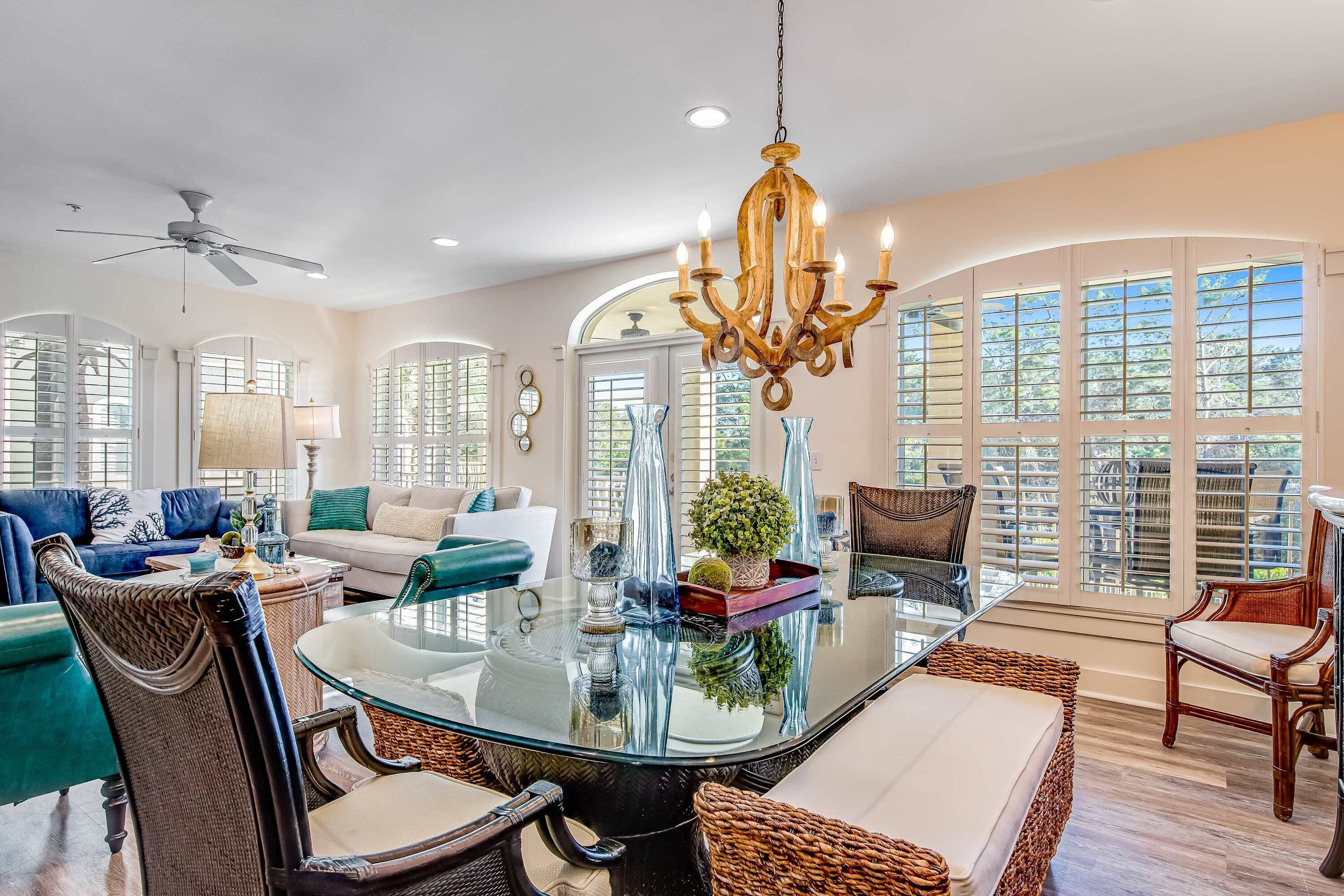 A spacious living room with a glass-top dining table, wicker chairs, and a chandelier.