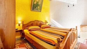 A wooden bed with a striped bedspread, a nightstand with a lamp, and a painting on the wall. - Apartment B with Private Terrace, Garden and Wi-Fi (Klausdorf)