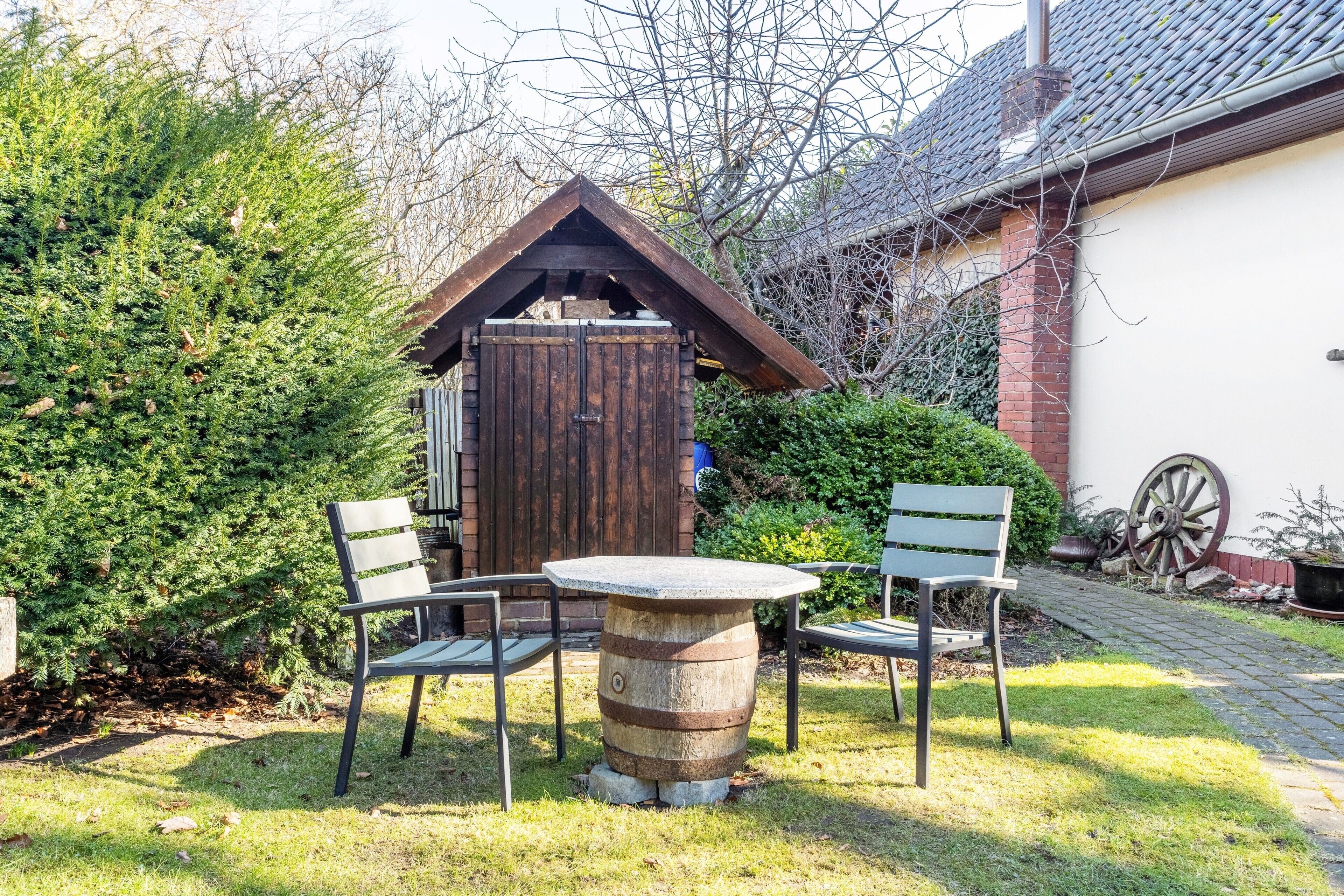 Un espace extérieur rustique aménagé avec une table en fût de bois, des chaises en métal et une structure en bois en arrière-plan.