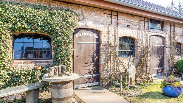 A building with ivy-covered walls, a stone bench, and a large wooden door labeled 'Fischstudio.' - Apartment B with Private Terrace, Garden and Wi-Fi (Klausdorf)