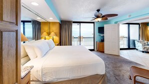 Habitación de hotel con una cama grande, ventilador de techo, balcón con vistas y escritorio con silla.