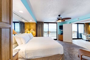 Een hotelkamer met een groot bed, een plafondventilator, een balkon met uitzicht en een bureau met stoel.