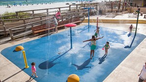Un área de juegos con agua que tiene una superficie azul, pelotas de seguridad amarillas y una terraza de madera con vistas a una playa.