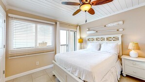 Quarto com cama, ventilador de teto, mesa de cabeceira e janela com persianas.