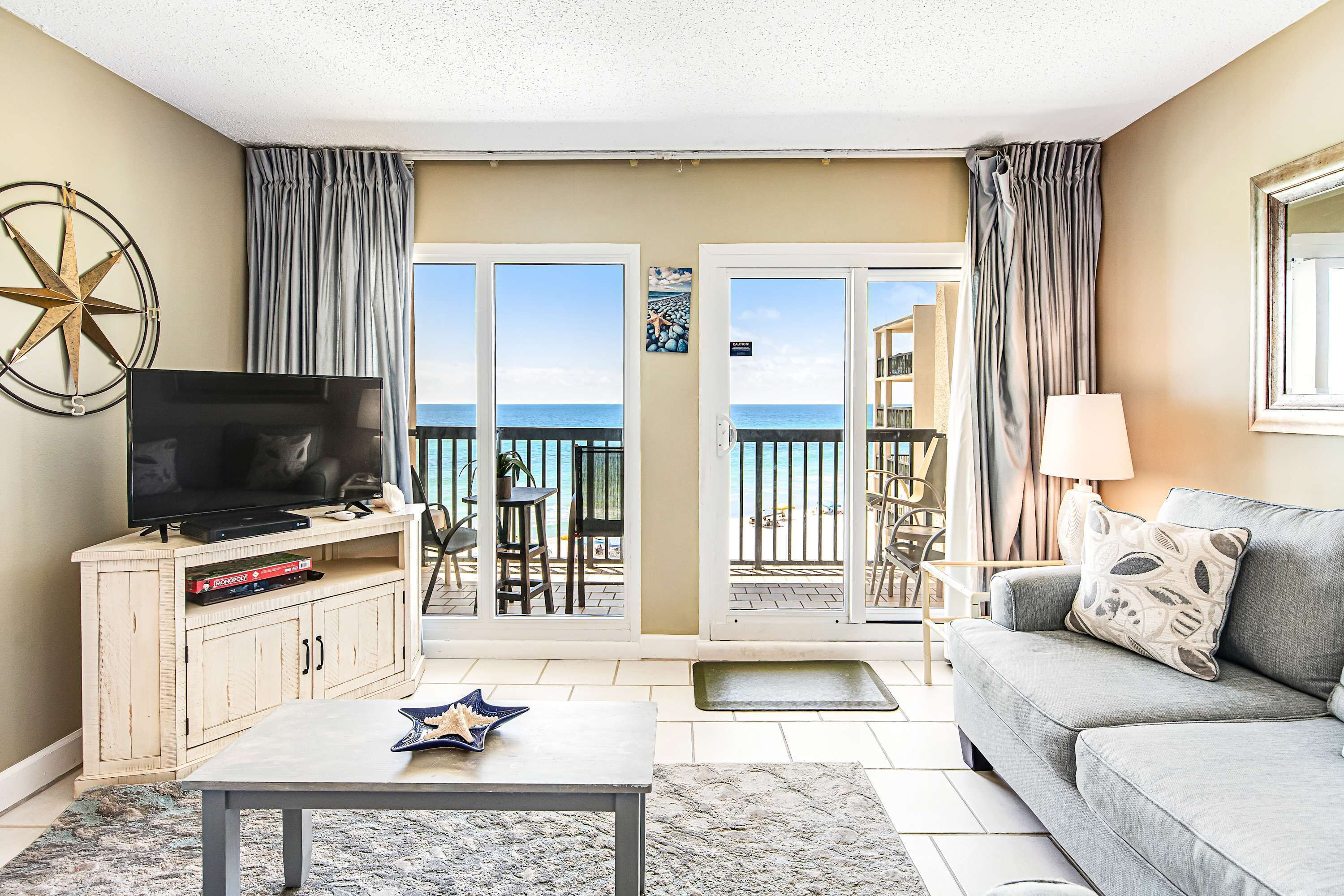 A living room with a television, a sofa, a coffee table, and a view of the sea through the sliding doors.