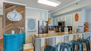 Una cocina con salpicadero de madera, un reloj, un refrigerador y una zona de bar con taburetes.