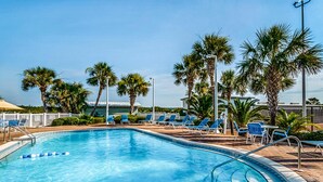 Una piscina con barreras flotantes azules y blancas, rodeada de sillones de descanso y palmeras.