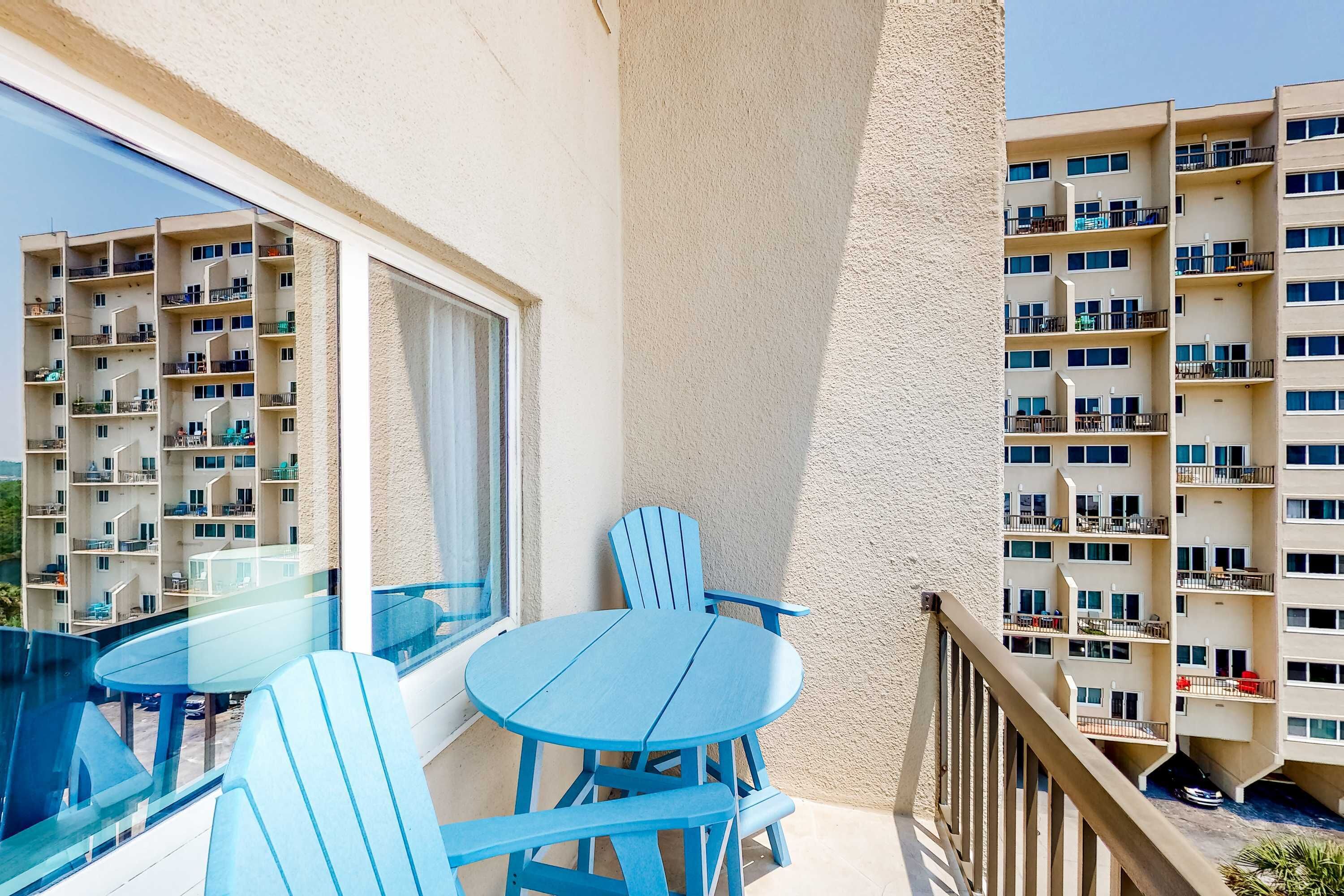A balcony with a round table and blue chairs, overlooking a residential building with multiple balconies.
