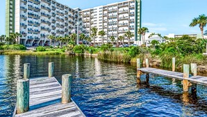Un hotel de varios pisos con un muelle que se adentra en el agua, rodeado de vegetación y palmeras.