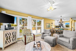 A living room with a flat-screen TV, a patterned armchair, two grey sofas, a coffee table, and a ceiling fan. - Oceanfront condo with outdoor pool, ocean view, high-speed WiFi & washer/dryer (Panama City Beach)