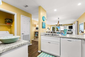 A modern kitchen with white cabinets, a granite countertop, and a built-in dishwasher. - Oceanfront condo with outdoor pool, ocean view, high-speed WiFi & washer/dryer (Panama City Beach)