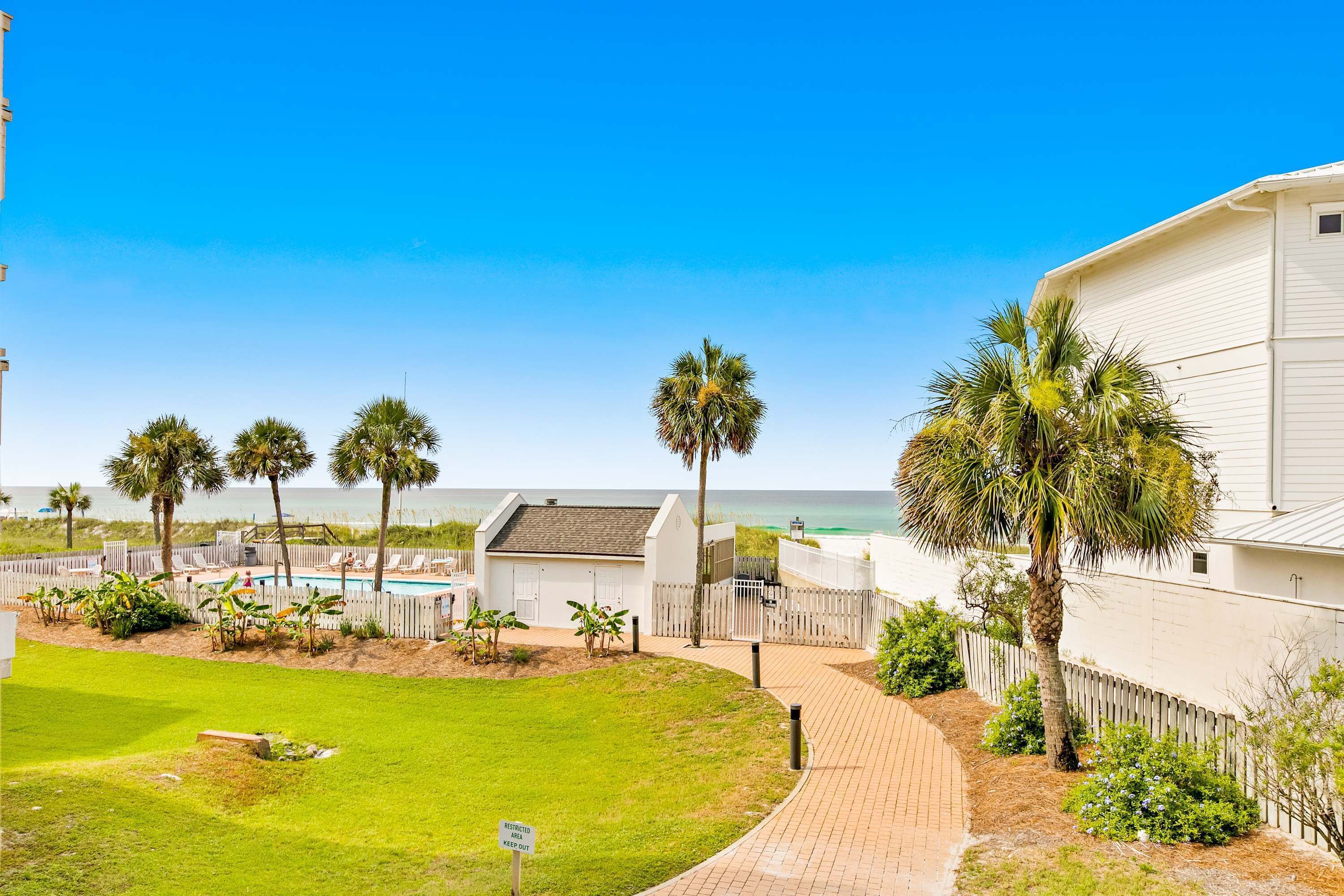 A beachfront property with a swimming pool, palm trees, and a view of the ocean.