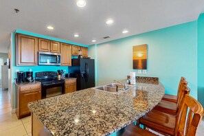 A kitchen with granite countertops, wooden cabinets, a black refrigerator, and a microwave. - Lovely beachfront resort condo with waterpark, pools, hot tub & beach access (Panama City Beach)