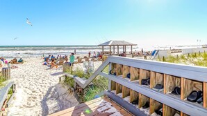 Ein Strand mit einer Holzpromenade, die zu Liegestühlen und Sonnenschirmen führt.