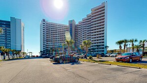 A parking lot with several cars, palm trees, and modern high-rise buildings in the background. - 16th floor condo with shared on-site pools, hot tub, restaurant, and bar (Destin)