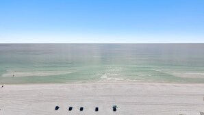 A beach with a clear sky, calm sea, and a few umbrellas on the sand. - 16th floor condo with shared on-site pools, hot tub, restaurant, and bar (Destin)