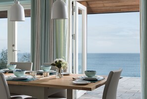 A dining table set with blue and white bowls, plates, and a vase with flowers, overlooking the sea. - Tredeanne - coastal retreat with breathtaking sea views (Veryan)
