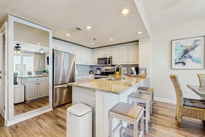 A modern kitchen with white cabinets, stainless steel appliances, and a granite countertop. - Elegant condo w water views, private balcony, shared fitness center and grills (Destin)