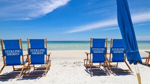 Des chaises de plage portant l’inscription « Sterling Shores » sont disposées sur une plage de sable, avec un ciel bleu clair et l’océan en arrière-plan.