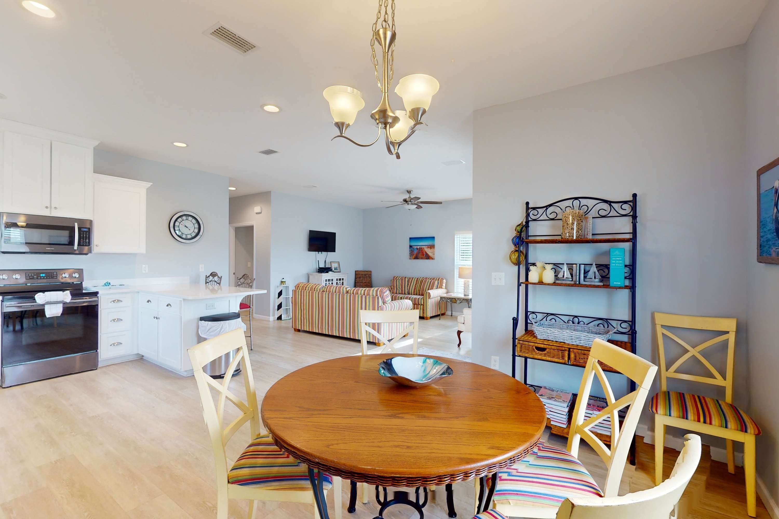 A modern kitchen with white cabinets, a microwave, and a stove. There is a dining area with a wooden table and striped chairs.