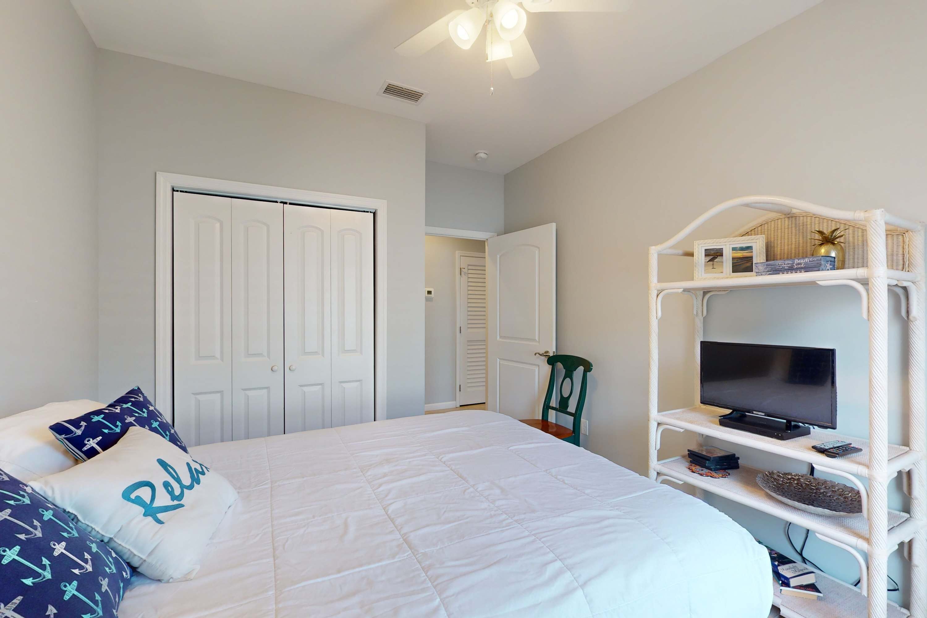 A bedroom with a bed, white walls, a ceiling fan, and a TV on a white stand.