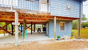 A two-story blue house with a covered porch, a wooden deck, and a small garden area with potted plants. - 2-story house near the beach & ocean with deck, golf cart, washer&dryer, AC (St. George Island)