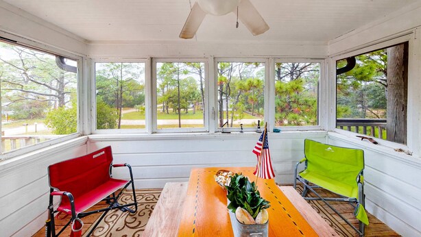 A room with a wooden table, two chairs, a ceiling fan, and large windows with a view of trees and a pathway. - 2-story house near the beach & ocean with deck, golf cart, washer&dryer, AC (St. George Island)