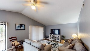 A living room with two grey sofas, a wooden rocking chair, a ceiling fan, a television, and a cabinet. - 2-story house near the beach & ocean with deck, golf cart, washer&dryer, AC (St. George Island)