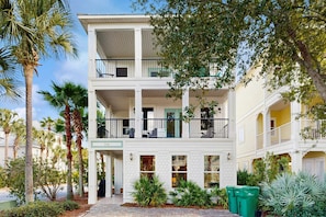 A multi-story hotel with balconies, a covered entrance, and a landscaped garden with palm trees. - Three-Story Home w/Washer/Dryer, Gas Grill, Central A/C, & Shared Pool, Hot Tub (Destin)