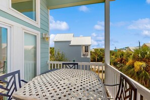 A balcony with a round table and chairs, a railing, and a view of a house and palm trees. - Dog-friendly Private home with gulf view, golf cart and easy beach access (Port St. Joe)