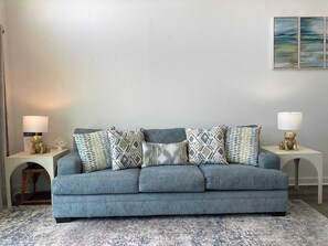 A blue sofa with patterned cushions, two bedside tables with lamps, and a rug on the floor.