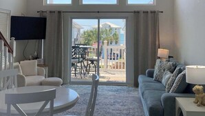 Un salón espacioso con ventilador de techo, un ventanal grande, una puerta corrediza de cristal que da a un patio exterior, un sofá, una mesa de centro y una mesa de comedor con sillas.