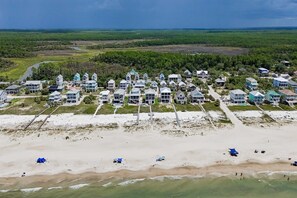 An aerial view of a coastal resort with multiple buildings, a sandy beach, and a clear view of the ocean.