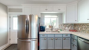 Una cucina moderna con mobili bianchi, un frigorifero in acciaio inossidabile e una parete rivestita in piastrelle.