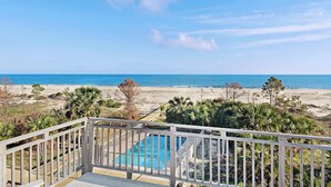 A pool with a wooden deck and railing, overlooking a beach with palm trees and the ocean. - Beachfront home with screened porch with boardwalk access to pool (Cape San Blas)